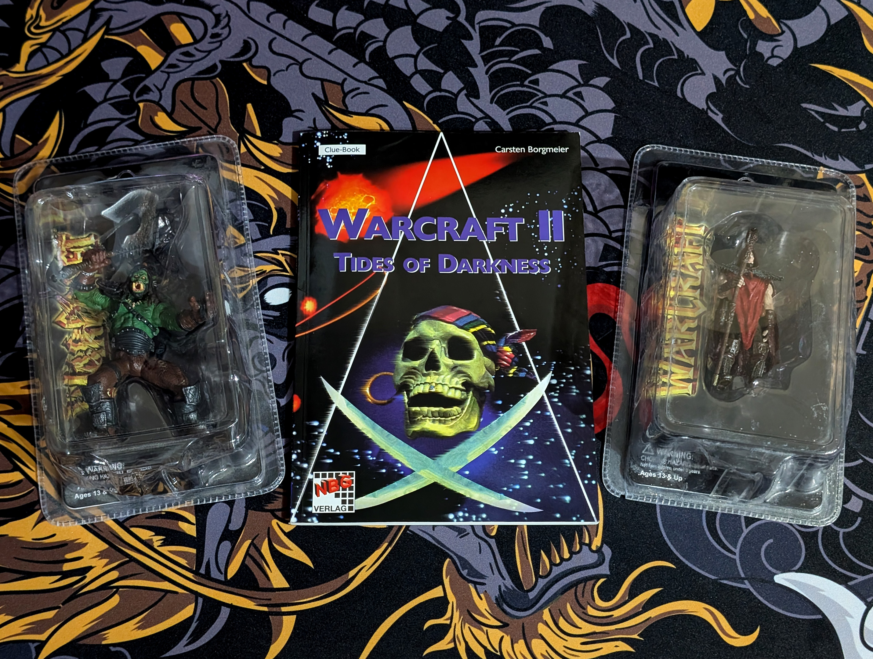 An unofficial German strategy guide and two licensed 'WarCraft Battle Collection' figures (Grom Hellscream and Medivh)